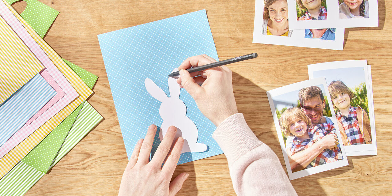 Dvije ruke nacrtaju uskrsnog zeca na papiru pomoću predloška. Pokraj njega su izrađene trenutne fotografije obitelji.