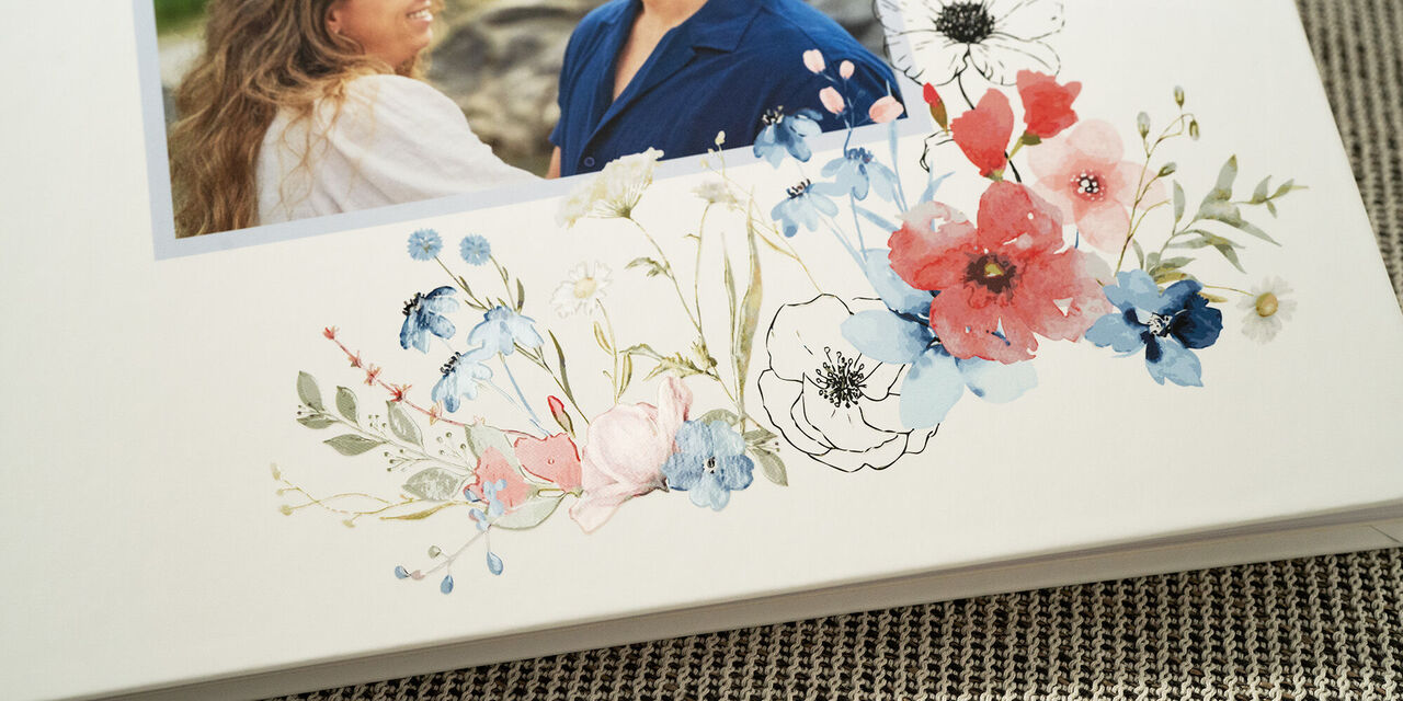 Krupni plan naslovnice knjige gostiju s fotografijom mladog para. Knjiga je elegantna s cvjetnim dizajnom vjenčanja i sjajnim efektima na bijeloj pozadini.